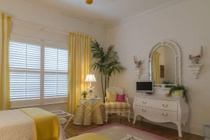 yellow-themed bedroom with white shutters and green corner plant