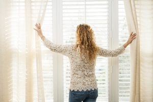 Women opening curtains of window with white blinds