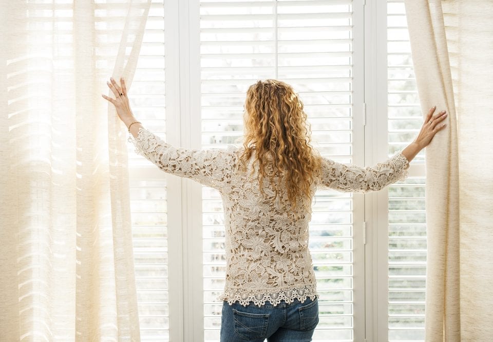 Women opening curtains of window with white blinds