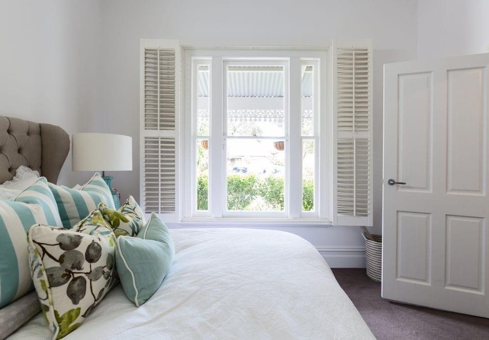 Bedroom window with a garden view through timber shutters.