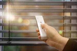 Venetian blind covering window with woman using remote control