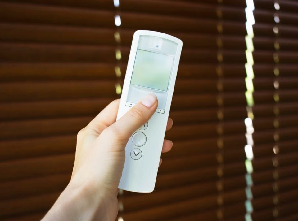 Hand holding remote control to open wooden blinds